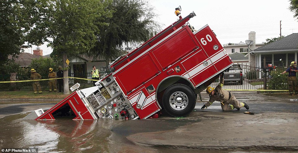 FILE - In this Tuesday, Sept. 8, 2009 file photo, a Los Angeles firefighter looks under a fire truck stuck in a sinkhole in the Valley Village neighborhood of Los Angeles. Four firefighters escaped injury early Tuesday after their vehicle sunk into the hole caused by a burst water main in the San Fernando Valley, authorities said. (AP Photo/Nick Ut).